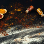 A variety of colorful spices, Salt and Vinegar Seasoning and measuring spoons are arranged on a black surface.